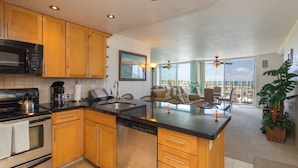 A modern kitchen with wooden cabinets, a built-in microwave, and a dishwasher. There is a large island with a sink and a seating area with a view of the ocean.