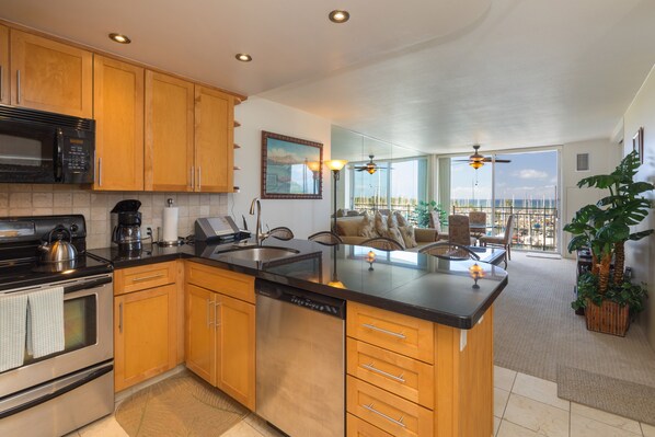 Cocina moderna con armarios de madera, microondas integrado y lavavajillas. Cuenta con una isla grande con pileta y una zona de estar con vista al océano.