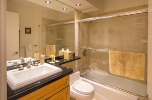 A modern bathroom with a large mirror, two sinks, a toilet, and a glass-enclosed shower.