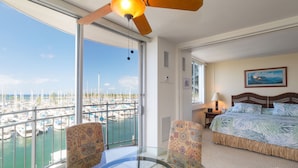 A hotel room with a balcony, a bed, a glass table, and a view of a marina.