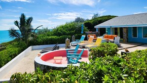 A pool area with colorful lounge chairs and a circular seating area, surrounded by lush greenery and a view of the ocean.
