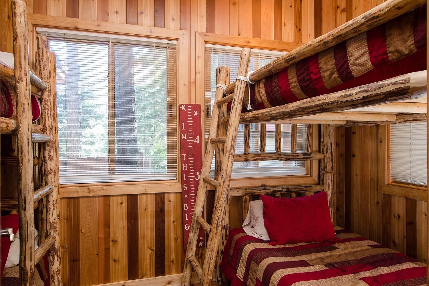 A rustic cabin with a loft bed, wooden walls, and a window with blinds.