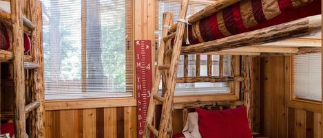 A rustic cabin with a loft bed, wooden walls, and a window with blinds.