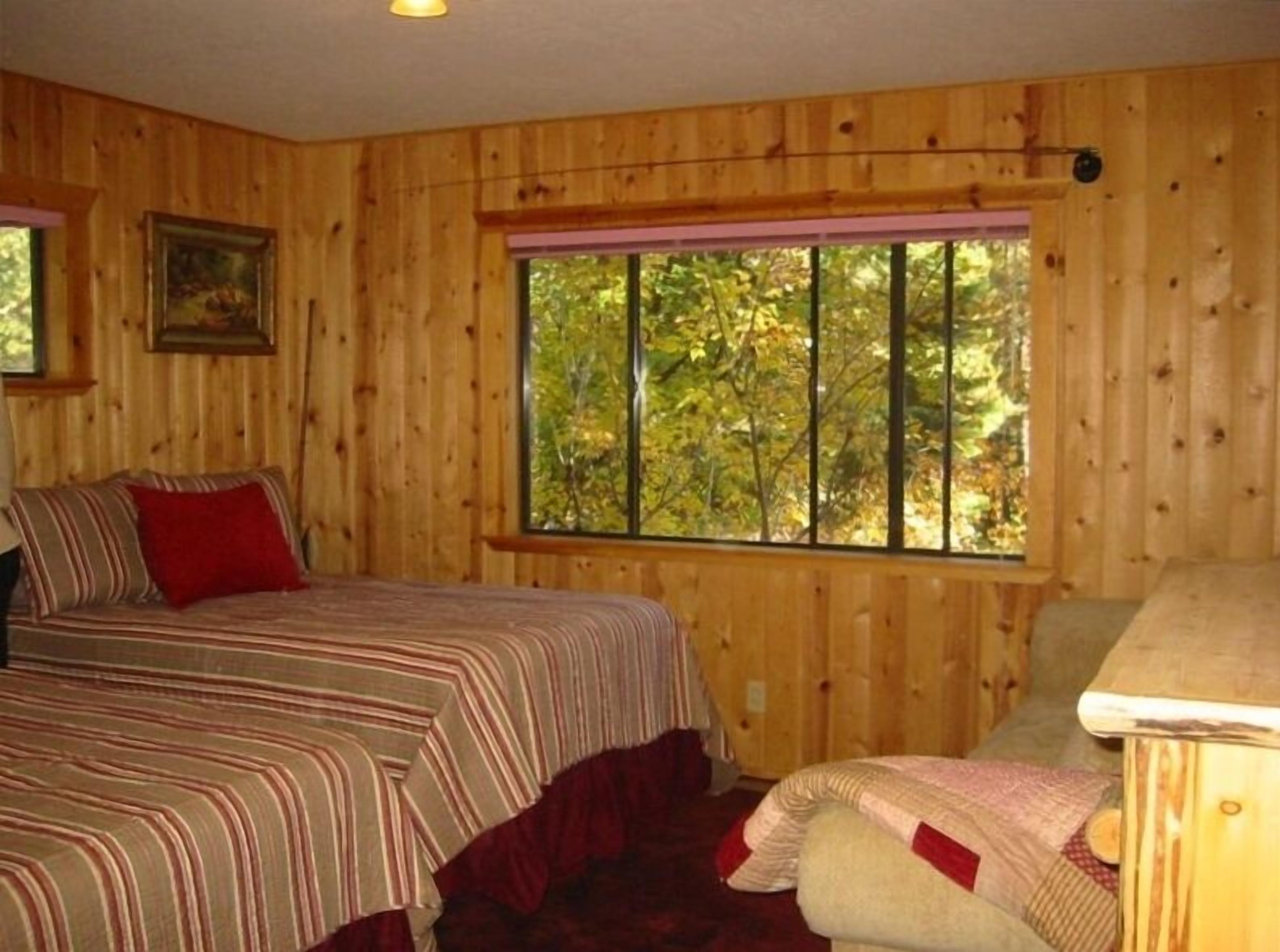 A wooden-paneled room with a bed, a window with a view of trees, and a small table.