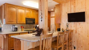 A kitchen with wooden cabinets, a microwave, a coffee maker, a squirrel statue, and a TV mounted on the wall. - Fabulous Cabin Block away from<br>Private Beach (Tahoe City)