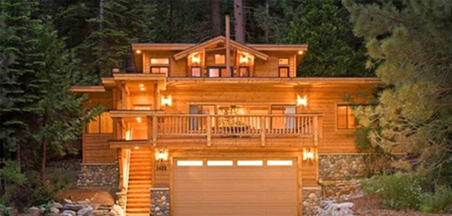 A large, two-story wooden cabin with a balcony, surrounded by trees.