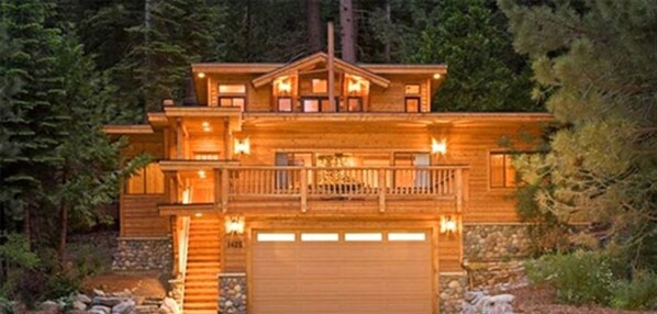 Une grande cabane en bois à deux étages, dotée d’un balcon et entourée d’arbres.