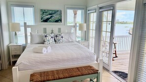 A bedroom with a bed, pillows, a bench, a nightstand, a lamp, and a view of a body of water through a window. - Finest location in Coral Lagoon.  End unit with open water bay and marina views. (Marathon)