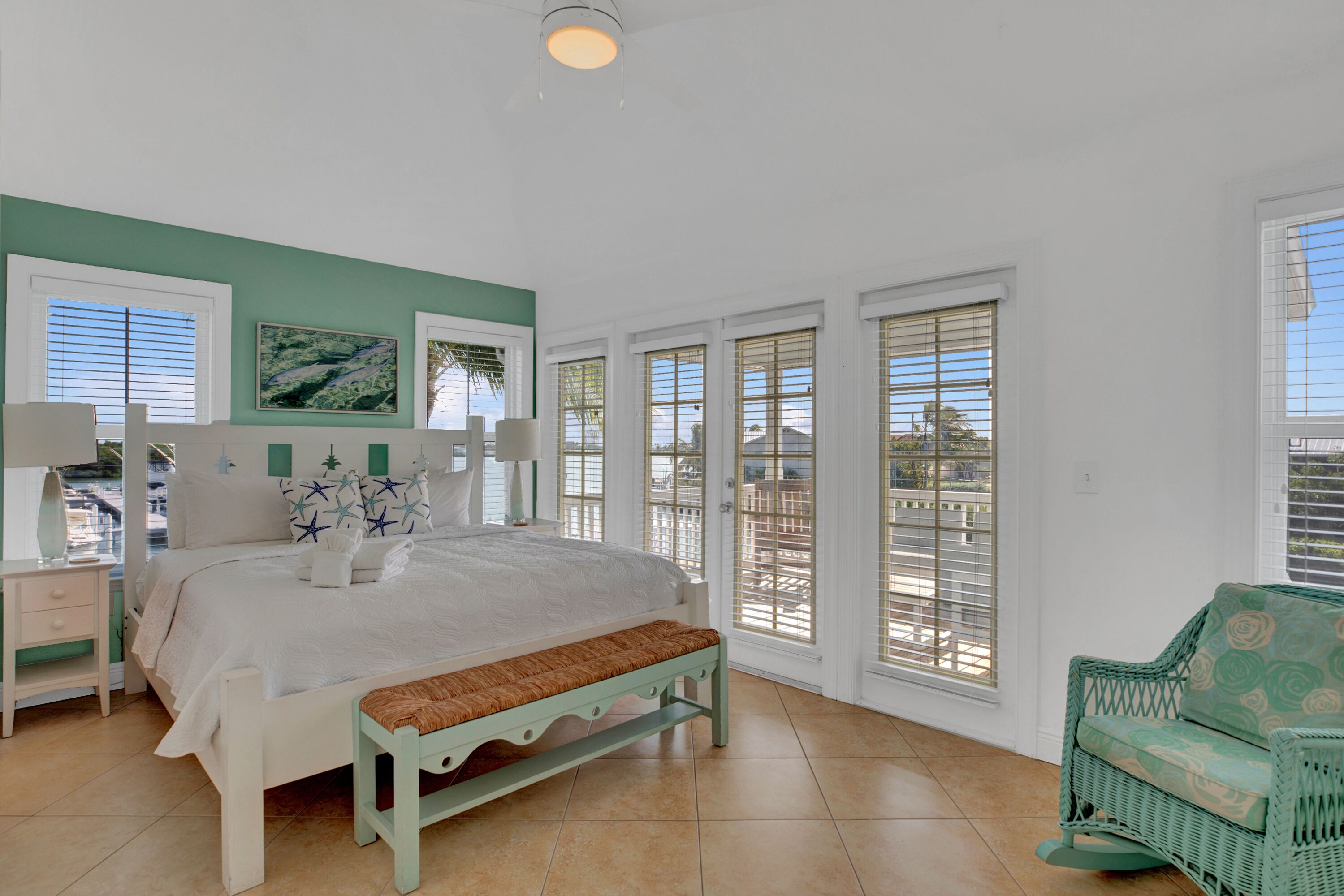 A bedroom with a bed, a bench, a chair, and large windows.