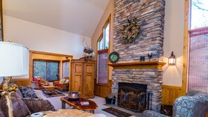 A cozy living room with a stone fireplace, wooden furniture, and a large window. - Charming 3BR / 3BA With Hot Tub, Fireplace & Pool Table (Galena)