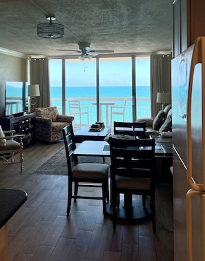 Una habitación con vistas al océano, un ventilador de techo, un televisor, una mesa de comedor con sillas y un sofá.