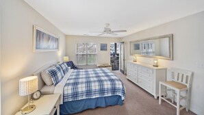 Quarto com cama, mesa de cabeceira, abajur, cômoda, cadeira e ventilador de teto.