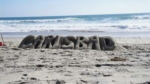 Una playa con una escultura de arena que dice "CINCHADA" y olas al fondo.