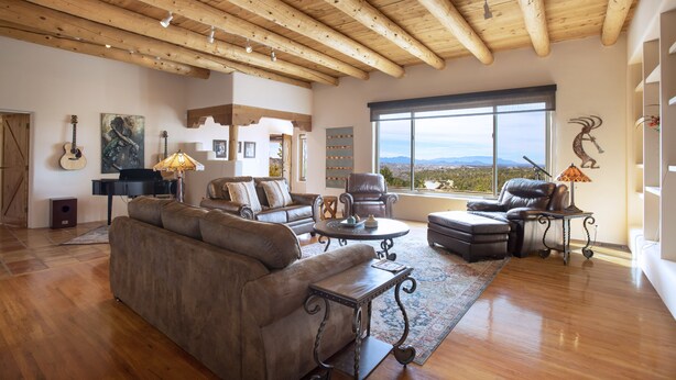 Un salón amplio con techo de madera alta, sofás de cuero, una mesa de centro y un ventanal con vistas al paisaje.