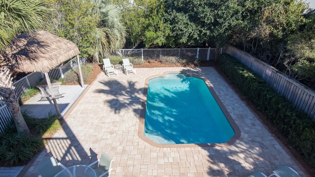 A rectangular swimming pool with a tiled deck, surrounded by a metal fence, and shaded by trees. - Lovely Coral Reef  5 B/R, 5 Bath, Private Pool. (Santa Rosa Beach)