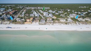 Oversigtsbillede af et kystnære boligområde med huse, en strand og klart turkis vand.