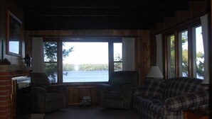 A cozy living room with a fireplace, a plaid sofa, and a view of a lake. - Secluded 2 acre Lakeside Home, boat & motor included on 5 lake chain. free Wi-Fi (Eagle River)