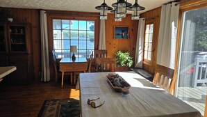 A wooden cabin interior with a dining table, chairs, a lamp, a potted plant, and a view of a lake through large windows. - Secluded 2 acre Lakeside Home, boat & motor included on 5 lake chain. free Wi-Fi (Eagle River)