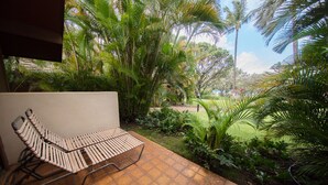 Un patio con una silla lounge de madera, rodeado de abundante follaje y vistas a un jardín.