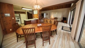 Un comedor con una mesa y sillas de madera, una araña y una cocina al fondo.
