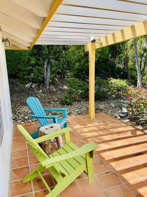 A covered patio area with a pergola, two Adirondack chairs, and a small table.