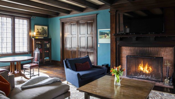 Un salon chaleureux avec une cheminée, des poutres en bois, un mur bleu et un coin salon confortable.