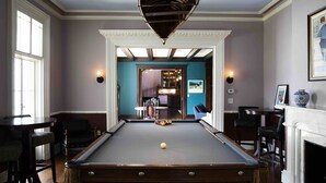 Une table de billard avec une bille au centre, entourée de tabourets de bar et d’une cheminée.