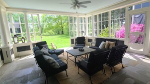 Une véranda dotée d’une grande porte vitrée, d’un ventilateur de plafond et d’un coin salon avec une table et des chaises.