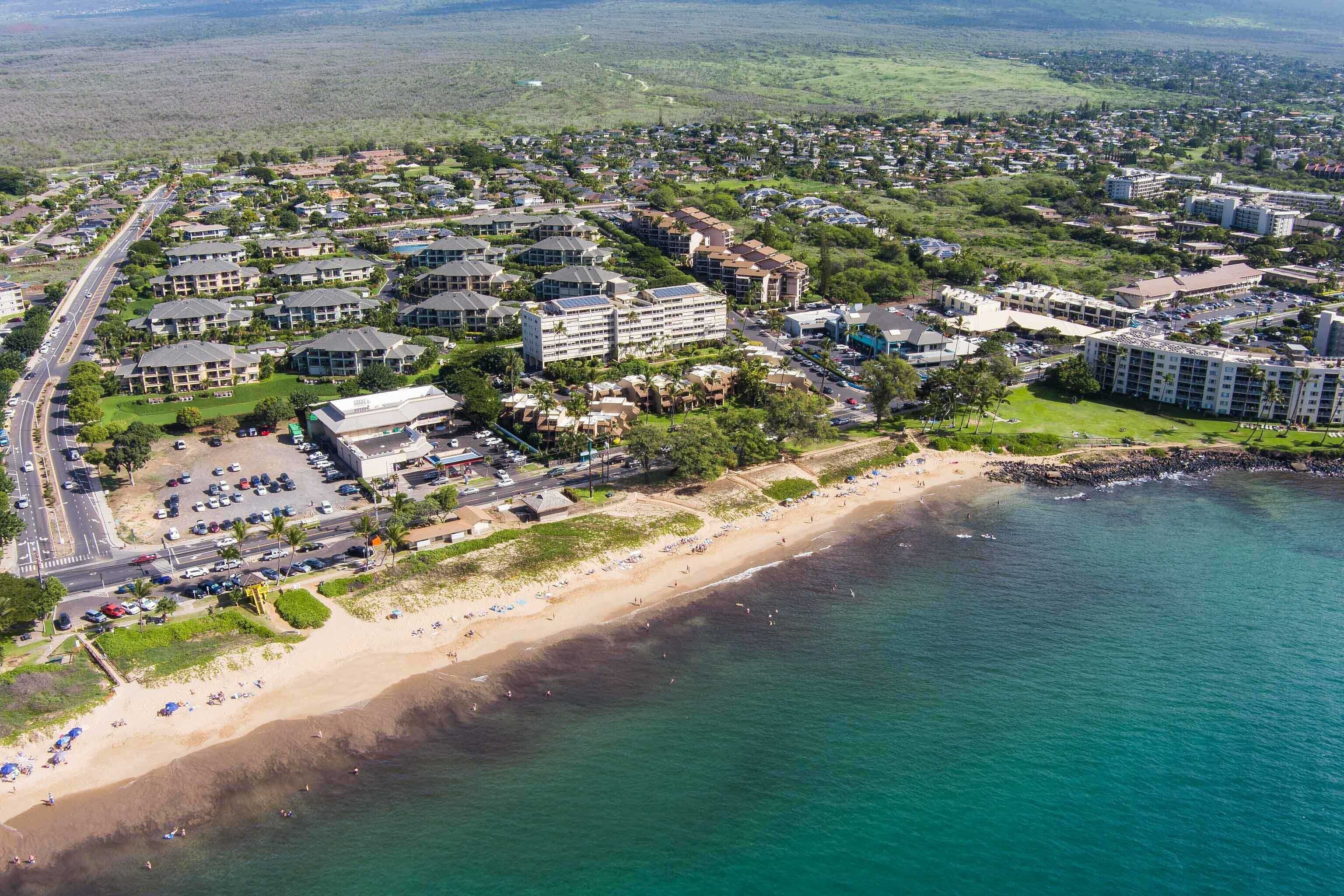 Vue aérienne d’une station balnéaire comprenant plusieurs bâtiments, une plage et un parking.