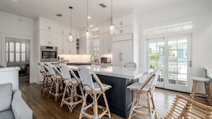 A modern kitchen with white cabinetry, a central island with bar stools, and pendant lighting. - Luxe gulf side living between Rosemary & Alys - walk to beach & oceanfront pool  (Panama City Beach)