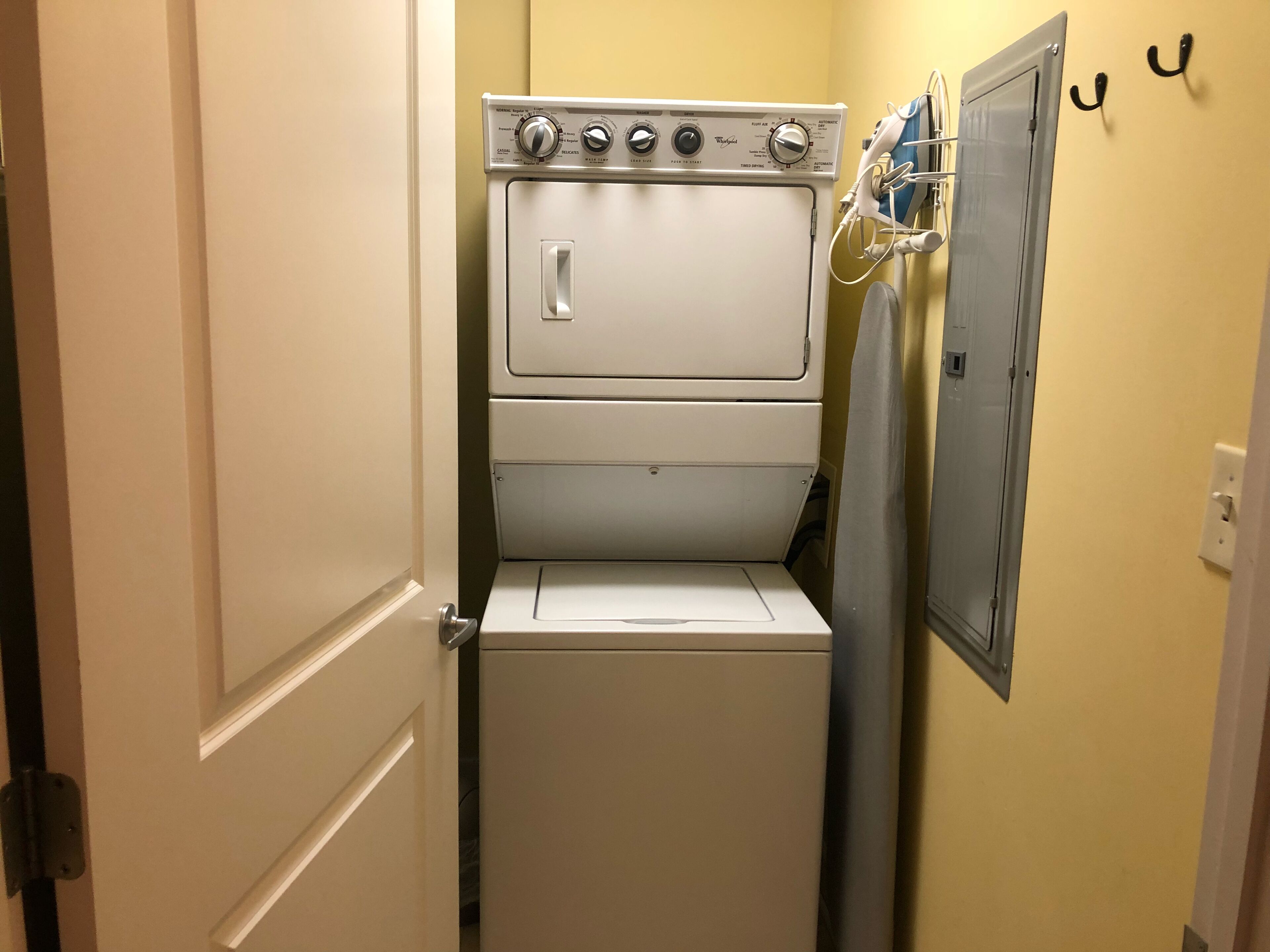 A compact laundry room with a front-loading washer and dryer, a door, and a wall-mounted rack.