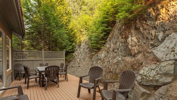 Une terrasse en bois, agrémentée de chaises et d’une table, entourée d’une falaise rocheuse et d’un feuillage dense.