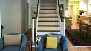 A living room with two blue armchairs, a wooden coffee table, and a staircase leading to a kitchen.