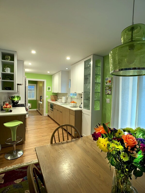 Una cocina moderna con comedor, que incluye una mesa de madera, un florero y una lámpara colgante verde.