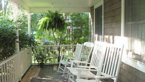 A wooden porch with white rocking chairs and a white railing.