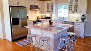 Une cuisine moderne avec des meubles blancs, un réfrigérateur en acier inoxydable, une cuisinière encastrée et un îlot central doté de tabourets de bar.
