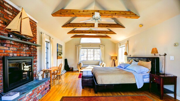 Une chambre avec une cheminée, des poutres apparentes, un lit et une fenêtre.