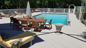 Une terrasse au bord de la piscine, avec des chaises longues, une table et un pot de fleurs.