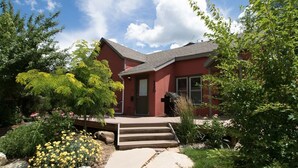 A red house with a stone pathway leading to the front door, surrounded by greenery and a clear sky. - Purple Juniper: Downtown witth Sunny Front Deck (Durango)