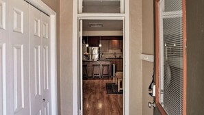 A hallway leading to a kitchen with wooden flooring, a refrigerator, and bar stools. - Purple Juniper: Downtown witth Sunny Front Deck (Durango)