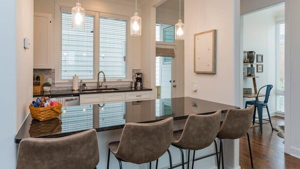 Una cucina moderna con isola centrale, luci a sospensione e zona pranzo con sgabelli da bar.