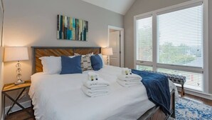 Camera d'albergo con un letto grande, due lampade ai comodini, una testiera in legno, una coperta azzurra e vista attraverso le persiane.