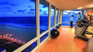 A gym with large windows overlooking a beach at dusk.
