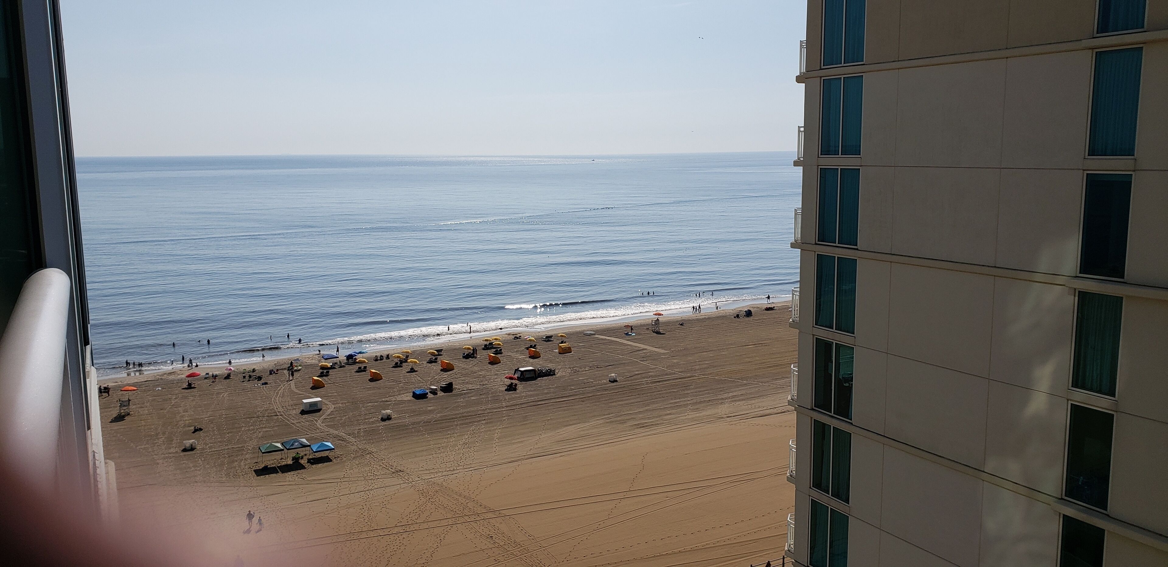Une vue sur la plage depuis un immeuble de grande hauteur, avec un ciel dégagé, une plage de sable, des parasols et des gens.