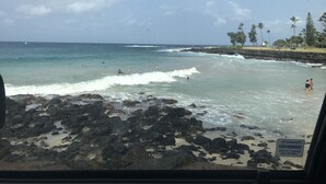 En strand med stenet kystlinje, bølger og mennesker i vandet.