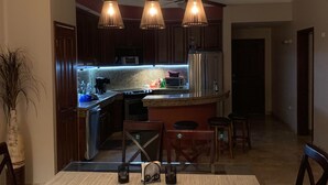 A modern kitchen with a central island, wooden chairs, and pendant lighting. - 2 BR condo nestled between Pacific Ocean beach and golf course    (Mazatlan)