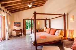 A four-poster bed with a wooden frame, a desk with a lamp, and a wicker chair.