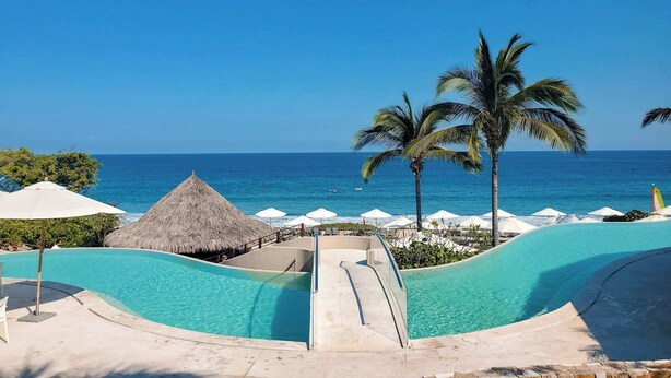 A resort pool with a slide, palm trees, and a view of the ocean. - Luxury Villa, Panoramic Views, Infinity Pool & Concierge (Punta Mita)