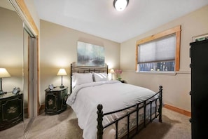 A bedroom with a bed, two bedside tables with lamps, a window with blinds, and a painting on the wall.