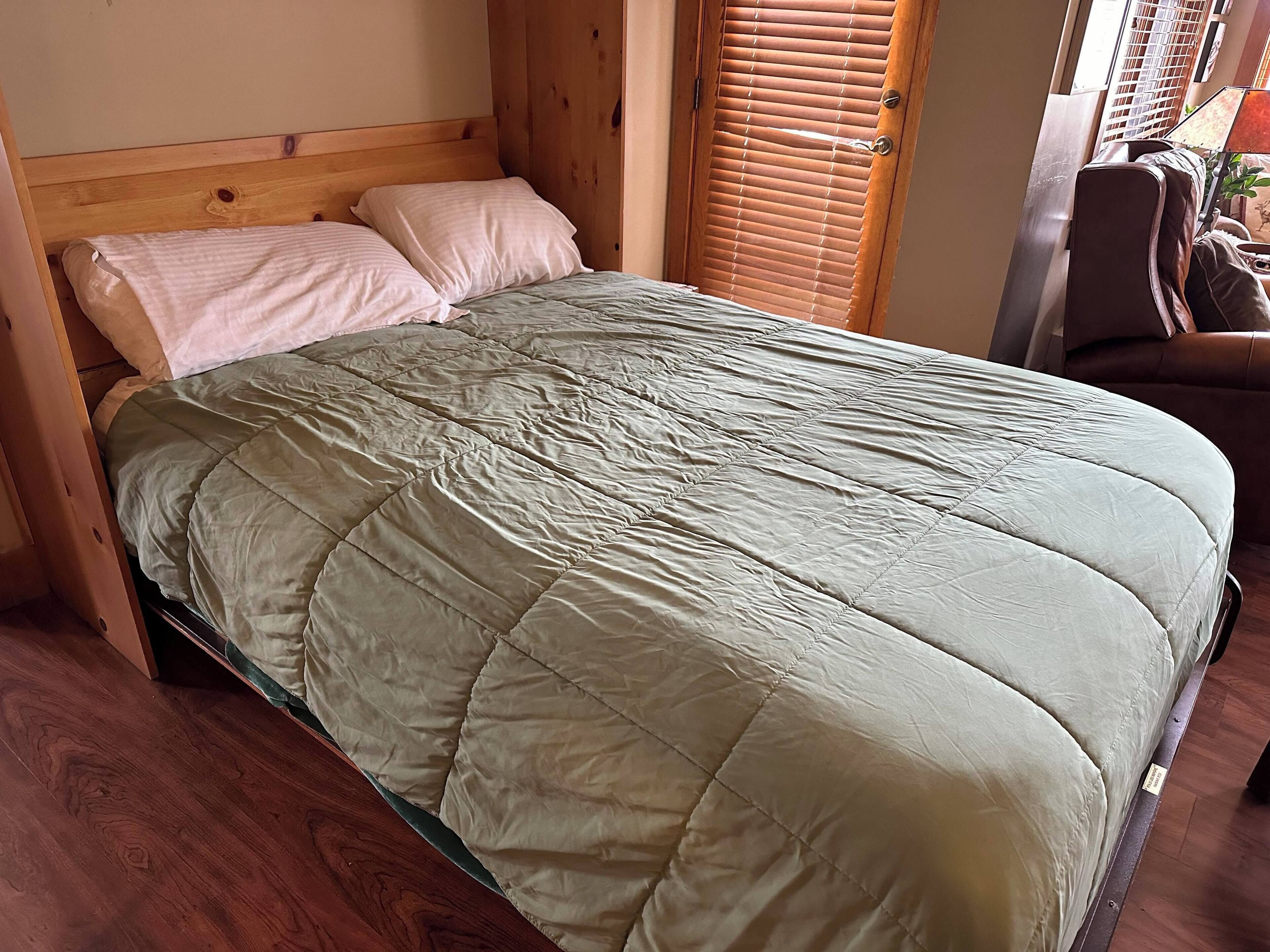 Un lit recouvert d’une courtepointe verte, avec une tête de lit en bois et un plancher en bois.